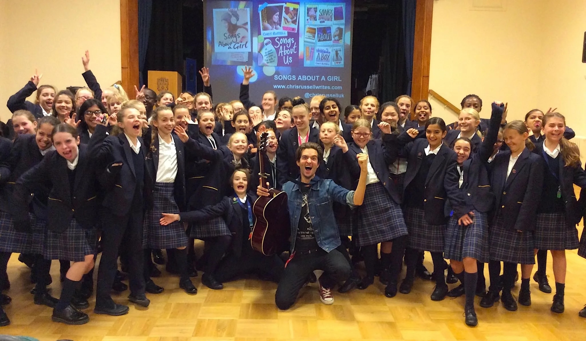 Chris Russell performing for students with a guitar in a school hall
