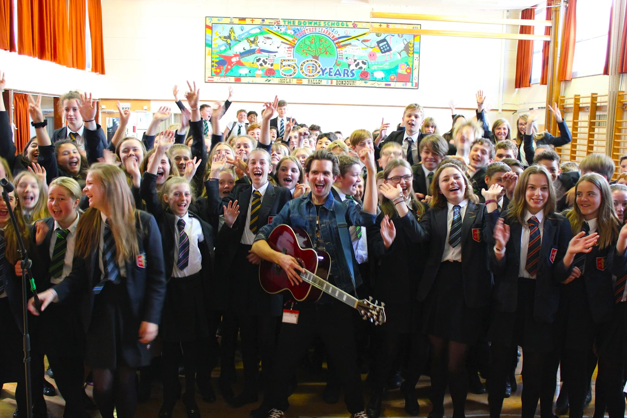 Chris Russell performing with a guitar for a school hall of cheering students